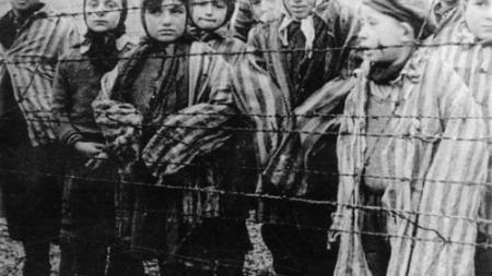 Children in striped prison uniforms behind fence at Auschwitz liberation